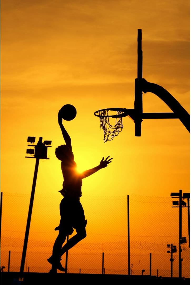 Silhouette of a basketball player leaping to dunk at sunset