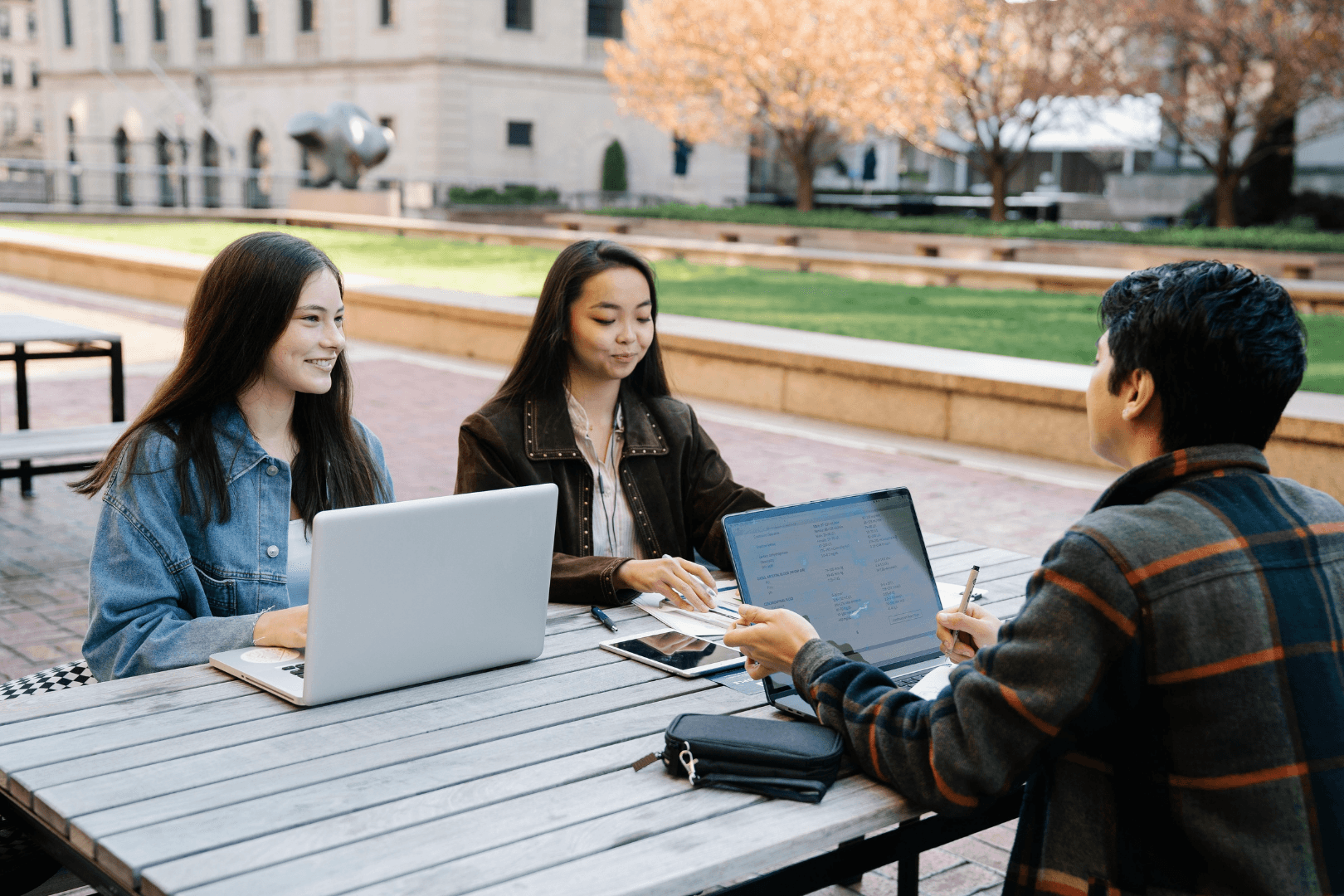 Students working together on laptops at an outdoor table on a college campus